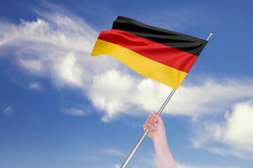 Female Hand is Waving German Flag Against Blue Sky with Clouds