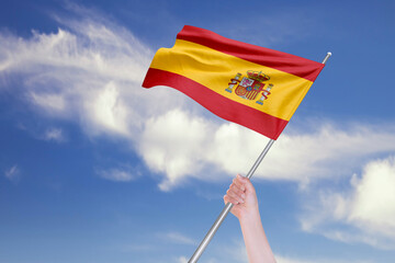 Female Hand is Waving Spanish Flag Against Blue Sky with Clouds