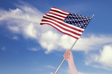 Female Hand is Waving USA Flag Against Blue Sky with Clouds