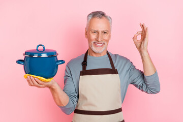 Photo of funny sweet man pensioner dressed grey shirt apron holding saucepan okey sign isolated...