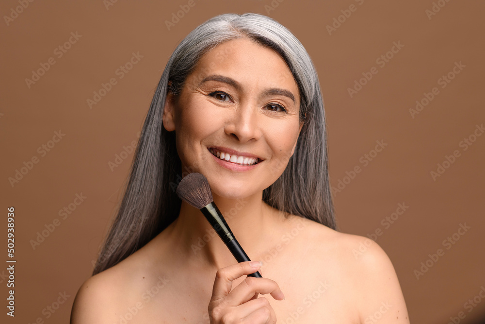 Poster take care of yourself. charming middle-aged asian woman standing with make-up brush isolated on brow