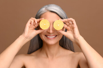 Fun portrait of middle-aged gray-haired half-naked Asian female covering eyes with halves of lemon...