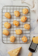 Freshly baked homemade cheese buns on a baking rack on a light marble background close-up. Brazilian cheese bread. A gourmet snack. Delicious pastries. Selective focus, top view - 502939373