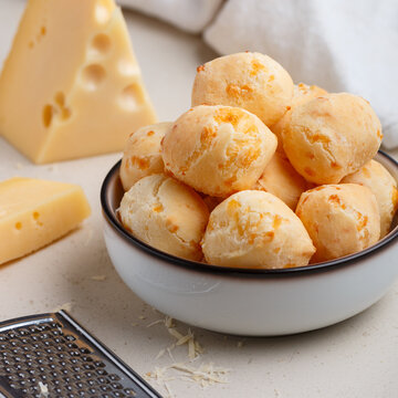 Freshly baked homemade cheese buns in a white plate on a light background close-up. A gourmet snack. Delicious pastries. Selective focus, square picture