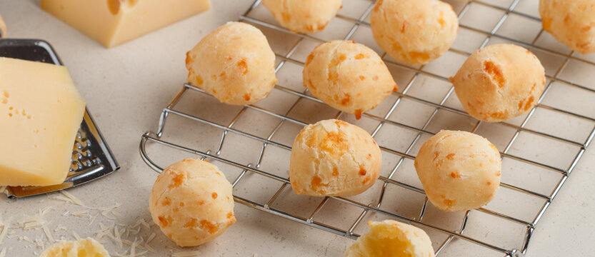 Freshly baked homemade cheese buns on a baking rack on a light background close-up. Brazilian cheese bread. A gourmet snack. Delicious pastries. Selective focus, banner