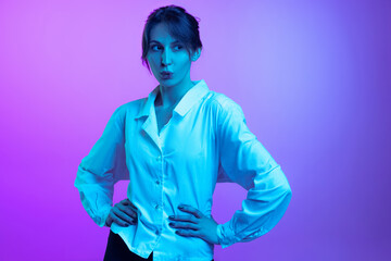 Portrait of pretty young girl in white shirt isolated over purple studio background in neon light. Concept of emotions, facial expression, art, beauty