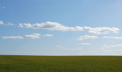 Fototapeta na wymiar White clouds in a light blue sky above the horizon of a green hillside landscape. 