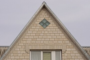 white bricks attic of a private house with a window against gray  sky
