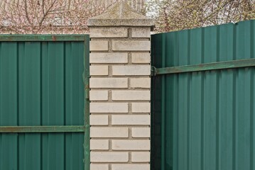 part of a fence wall made of white bricks and green metal on a city street