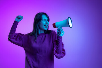 One young excited girl, student shouting at megaphone isolated over purple studio background in neon light. Concept of emotions, news, ad