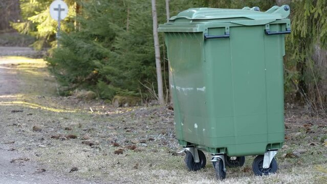 A green garbage bin on the side of the bushes in the forest in Estonia