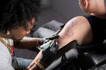 Professional African American tattoo artist makes a tattoo on client arm. High quality photography.