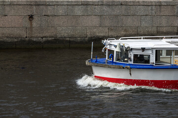 The nose of a ship floating along the river along the granite embankment cuts the water surface,...