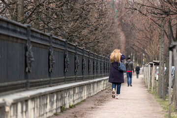 A girl with red hair walks along the fence and holds her head with her hands
