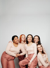 Group of attractive real women with different skins standing together and embracing against white wall