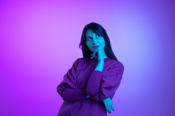 Studio shot of young attractive girl, student with long hair isolated over purple studio background in neon light. Concept of emotions, art, beauty