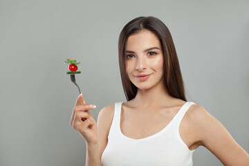 Cute woman with salad on fork smiling on white background