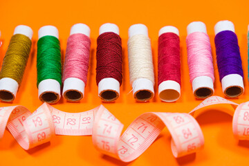 A set of multi-colored threads for sewing and a measuring tape on an orange background, top view....