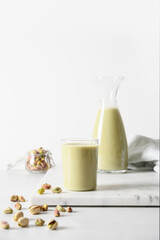 Pistachio milk in jug and pistachios on white background. Vegan plant based and lactose free milk. Vertical.