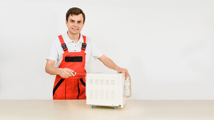 Repairman in red overall is fixing a microwave oven with a screwdriver on white background. .