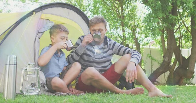 Animation of light spots over caucasian father and son drinking tea in tent in garden