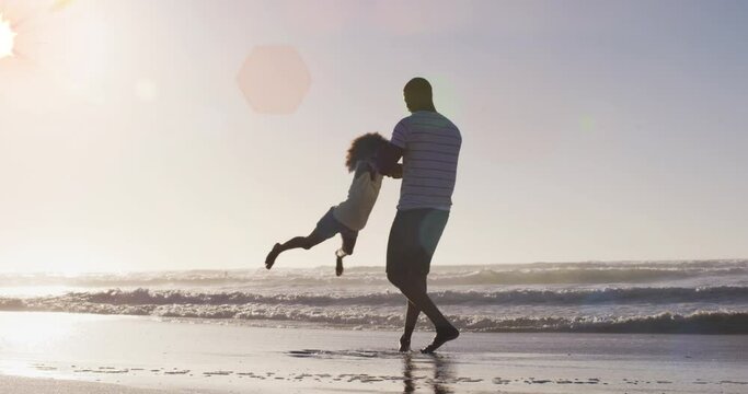 Animation of spots over happy african american father with daughter on sunny beach