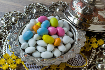 Traditional, white and pastel tones colored, chocolate covered almond candies in silver vintage bowl, on wooden surface