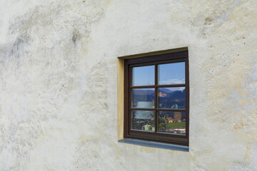 White stone wall with one old window with blue sky and mountains reflection