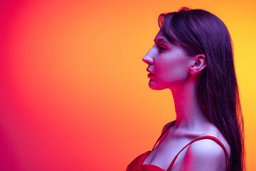 Profile view of young pretty girl with long glossy hair isolated over red-yellow background in neon light. Concept of emotions, facial expression, art, beauty