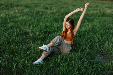 A woman lies on the green grass in the park with her legs up and having fun against the lawn, viewed from above. The concept of relaxing in nature and caring for the environment