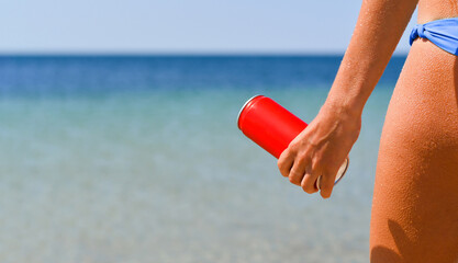 The girl holds in her hand a red can with a cold drink on the background of the sea.