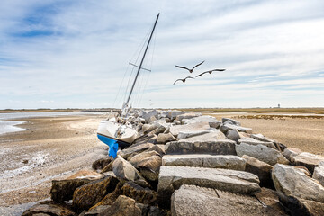 No water under the keel. Modern sailboat, yacht stranded on the beach besides a pier of rocks. East coast, Massachusetts - obrazy, fototapety, plakaty