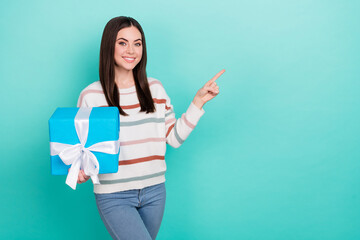 Photo of cute charming lady hold gift finger indicate empty space wear striped pullover isolated blue color background