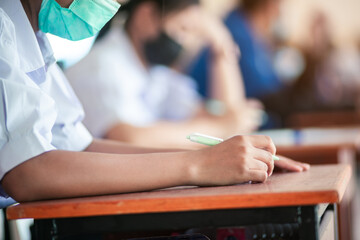 Student taking exam while wearing face mask due to coronavirus emergency. Young woman sitting in class with wearing surgical mask due to Covid-19 pandemic.