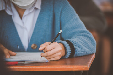 Student taking exam while wearing face mask due to coronavirus emergency. Young woman sitting in...