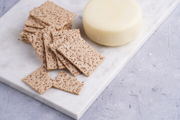 Healthy crunchy crisp crackers with sesame seeds and round cheese kashkaval on marble board