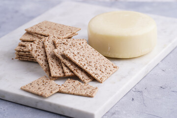 Healthy crunchy crisp crackers with sesame seeds and round cheese kashkaval on marble board