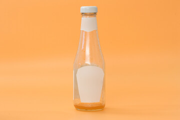 A dirty glass bottle of tomatoes ketchup with a white label and cap stands on a yellow background. Jar. Container. Clear. Small. Dirt. Empty Bottle. Ketchup. Used. Litter. Template