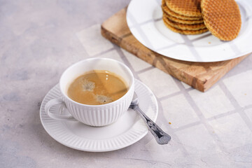 Stroopwafel - traditional dutch sirup waffles with caramel filling - stacked on top of each other on a wooden board, white kitchen and a cup of coffee in white porcelain cup