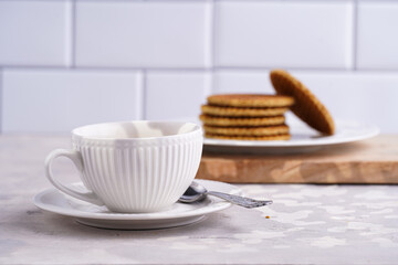 Stroopwafel - traditional dutch sirup waffles with caramel filling - stacked on top of each other on a wooden board, white kitchen and a cup of coffee in white porcelain cup
