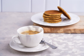 Stroopwafel - traditional dutch sirup waffles with caramel filling - stacked on top of each other on a wooden board, white kitchen and a cup of coffee in white porcelain cup