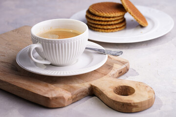 Stroopwafel - traditional dutch sirup waffles with caramel filling - stacked on top of each other on a wooden board, white kitchen and a cup of coffee in white porcelain cup