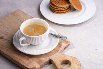 Stroopwafel - traditional dutch sirup waffles with caramel filling - stacked on top of each other on a wooden board, white kitchen and a cup of coffee in white porcelain cup