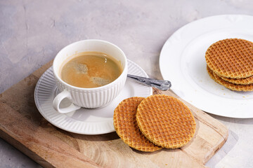Stroopwafel - traditional dutch sirup waffles with caramel filling - stacked on top of each other on a wooden board, white kitchen and a cup of coffee in white porcelain cup