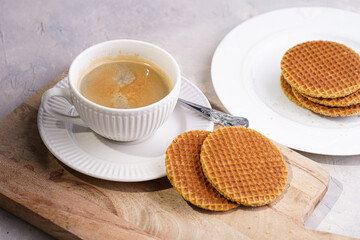 Stroopwafel - traditional dutch sirup waffles with caramel filling - stacked on top of each other on a wooden board, white kitchen and a cup of coffee in white porcelain cup