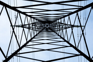 View from the bottom upwards to steel tower of electric main or electricity transmission line with the wires silhouette on background of cloudy blue sky