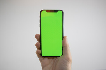 Holding an iPhone in hand. Green Screen on the phone. Mock-up of an iPhone. Apple product in hand. Vertical tilt of the phone.