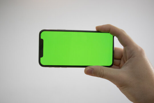 Holding An IPhone In Hand. Green Screen On The Phone. Mock-up Of An IPhone. Apple Product In Hand. Vertical Tilt Of The Phone.