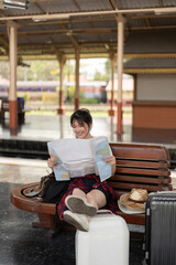 Fototapeta premium Happy young asian woman traveler or backpacker using map choose where to travel with luggage at train station, summer vacation travel concept