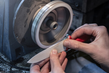 Knife sharpener and hand with blade. Man's hands sharpen a ceramic knife with a grinding wheel,...